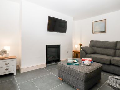 A living room with a grey sofa a grey ottoman a wall mounted TV and two side tables with lamps at Beach Road House in Hele Bay Ilfracombe