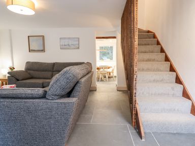 A living room with a grey sofa adjacent to carpeted stairs and a dining area visible through a doorway at Beach Road House in Hele Bay Ilfracombe
