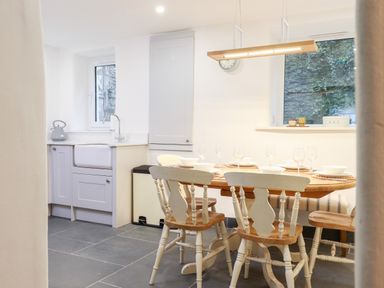 A kitchen with a wooden dining table set with bowls and glasses and chairs at Beach Road House in Hele Bay Ilfracombe