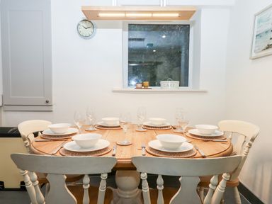 A wooden dining table set with white bowls plates and wine glasses in a kitchen at Beach Road House in Hele Bay Ilfracombe