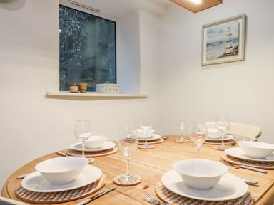 A dining table set with bowls plates wine glasses and cutlery in a room with a window and a painting at Beach Road House in Hele Bay Ilfracombe