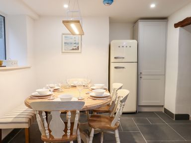 A dining room with a wooden table and chairs set with bowls and wine glasses and a cream refrigerator Beach Road House Hele Bay Ilfracombe