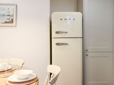 A kitchen area with a retro style SMEG refrigerator white chairs and a dining table set with plates bowls and glasses at Beach Road House in Hele Bay Ilfracombe