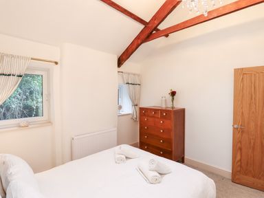 A bedroom with a bed with towels on it two windows a wooden dresser with flowers and a wooden door at Beach Road House in Hele Bay Ilfracombe