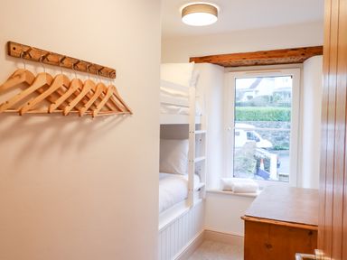 A small bedroom with bunk beds a wooden chest a window and wooden hangers on the wall at Beach Road House in Hele Bay Ilfracombe