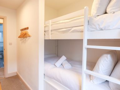 A bedroom with white bunk beds and wooden hangers on the wall at Beach Road House in Hele Bay Ilfracombe