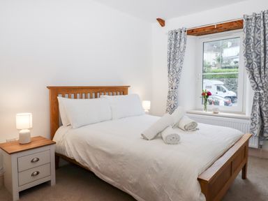 A bedroom with a wooden bed frame white bedding rolled towels bedside tables and a window with patterned curtains at Beach Road House in Hele Bay Ilfracombe