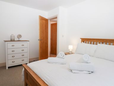 A bedroom with a wooden bed and white bedding and towels on the bed and a white chest of drawers with a vase and decorative item at Beach Road House in Hele Bay Ilfracombe