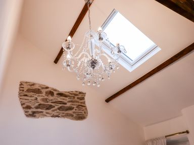 A ceiling with wooden beams a skylight and a crystal chandelier at Beach Road House in Hele Bay Ilfracombe