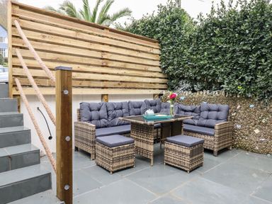 An outdoor seating area with wicker furniture and cushions next to stone steps and a wooden fence at Beach Road House in Hele Bay Ilfracombe