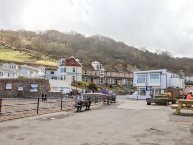 A promenade with benches and picnic tables near a pebble beach and buildings at Beach Road House in Hele Bay Ilfracombe