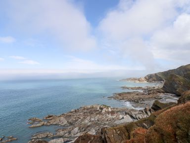 A rocky coastline with a calm sea and partly cloudy sky at Beach Road House in Hele Bay Ilfracombe