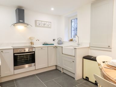 A kitchen with grey cabinets an oven a sink and a window at Beach Road House in Hele Bay Ilfracombe