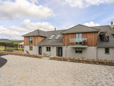 A modern house with stone driveway wood siding and glass balcony at Rynys in Llanddeiniolen near Llanrug