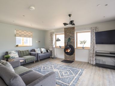 A living room with sofas a patterned rug a wall-mounted stove and a TV at Rynys in Llanddeiniolen near Llanrug