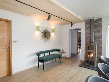 A room with a green bench a small side table a wall mirror and a wood burning stove at Rynys in Llanddeiniolen near Llanrug
