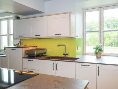 A kitchen with white cabinets a sink a green backsplash and a window with plants on the counter at Rynys in Llanddeiniolen near Llanrug