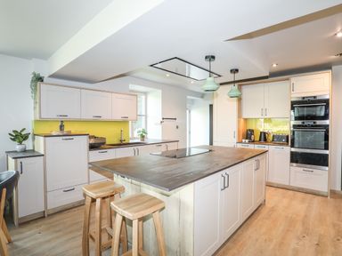 A kitchen with an island and wooden stools and white cabinets at Rynys in Llanddeiniolen near Llanrug