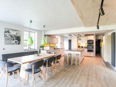 A kitchen and dining area with wooden table, gray chairs, green pendant lights, and kitchen island at Rynys in Llanddeiniolen near Llanrug
