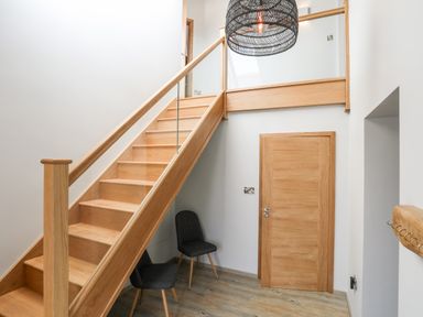 A wooden staircase with glass panel balustrade two black chairs a wooden door and a coat rack in an entryway at Rynys in Llanddeiniolen near Llanrug