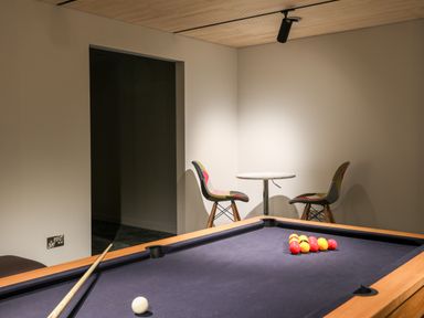 A pool table with balls and cue sticks near a small round table with two chairs in a game room at Rynys in Llanddeiniolen near Llanrug