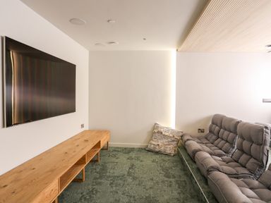 A room with a wall-mounted television a wooden low cabinet and a grey cushioned sofa at Rynys in Llanddeiniolen near Llanrug