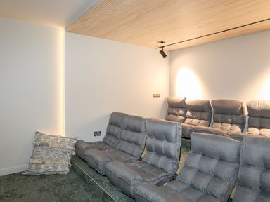 A home theater room with multiple gray cushioned seats and a wooden slatted ceiling at Rynys in Llanddeiniolen near Llanrug