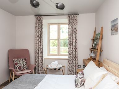 A bedroom with a bed pillow chair window with curtains and shelves at Rynys in Llanddeiniolen near Llanrug