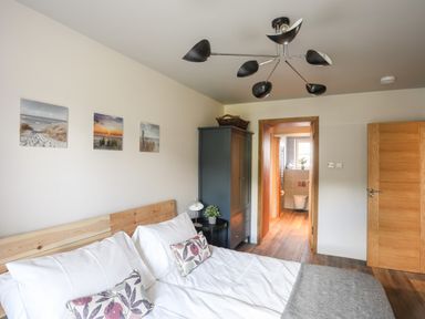 A bedroom with a double bed pillows and a wardrobe near a door leading to a bathroom at Rynys in Llanddeiniolen near Llanrug