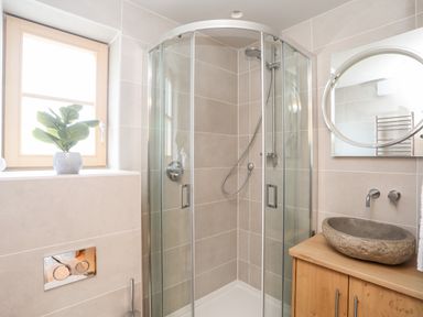 A bathroom with a corner glass shower enclosure a stone sink on a wooden cabinet and a small plant on the windowsill at Rynys in Llanddeiniolen near Llanrug