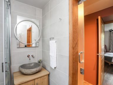 A bathroom with a round mirror stone sink towel rack and wooden cabinet at Rynys in Llanddeiniolen near Llanrug