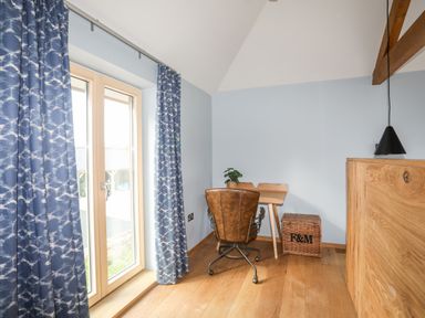 A corner with a wooden floor a small wooden desk a brown swivel chair blue patterned curtains and a wicker basket at Rynys in Llanddeiniolen near Llanrug