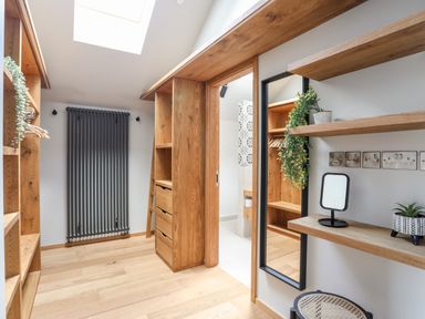 A walk-in closet with wooden shelves drawers a mirror and a small dressing table with plants and a stool at Rynys in Llanddeiniolen near Llanrug