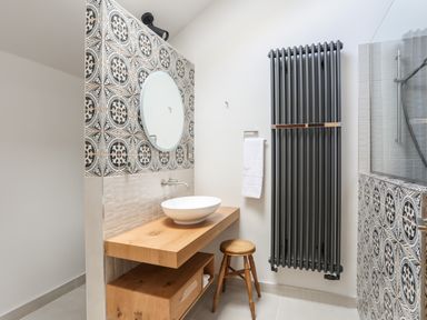 A bathroom with a wooden countertop and sink a round mirror black radiator and patterned tiles at Rynys in Llanddeiniolen near Llanrug