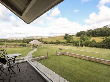 A balcony with a metal table and two chairs overlooking a lawn with a gazebo and trees at Rynys in Llanddeiniolen near Llanrug