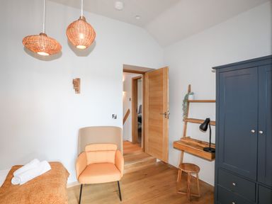 A room with a beige armchair a wooden desk and stool a dark blue wardrobe and an open wooden door at Rynys in Llanddeiniolen near Llanrug