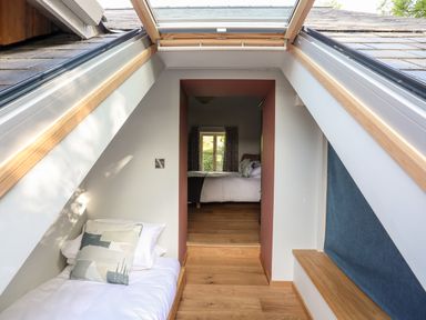 A small bedroom with a bed under skylight windows and a view into another bedroom at Rynys in Llanddeiniolen near Llanrug