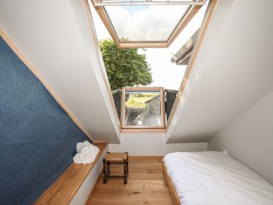 A small bedroom with a bed a stool and an open skylight window showing a tree and stone wall at Rynys in Llanddeiniolen near Llanrug