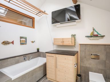 A bathroom with a bathtub wooden cabinets TV and nautical decorations at Rynys in Llanddeiniolen near Llanrug