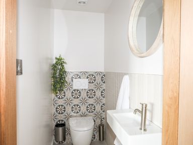 A bathroom with a toilet a sink a round mirror and patterned tiles behind the toilet at Rynys in Llanddeiniolen near Llanrug