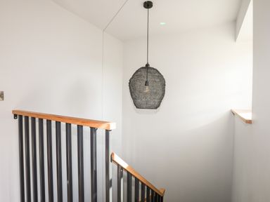 A staircase with black vertical railings and a wooden handrail with a hanging light fixture at Rynys in Llanddeiniolen near Llanrug