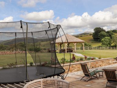 An outdoor area with a trampoline chairs a wooden gazebo and a stone wall at Rynys in Llanddeiniolen near Llanrug