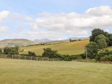 A grassy field with a wooden fence trees and rolling hills in the background at Rynys in Llanddeiniolen near Llanrug