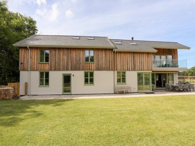 A two story house with wooden cladding and green windows and doors with a lawn in front at Rynys in Llanddeiniolen near Llanrug