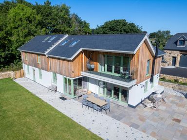 A modern two story house with wooden and white exterior walls a patio with chairs and tables and a grassy yard at Rynys in Llanddeiniolen near Llanrug