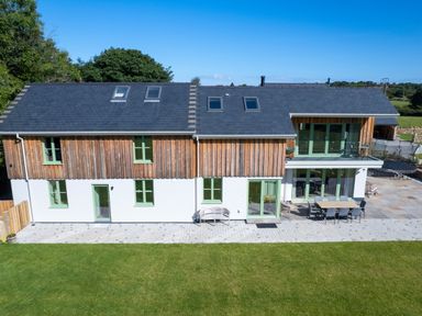A modern two-story house with wooden panels a garden and outdoor seating at Rynys in Llanddeiniolen near Llanrug