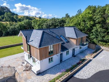 A two-story house with wooden paneling and tiled roof surrounded by trees and lawn at Rynys in Llanddeiniolen near Llanrug