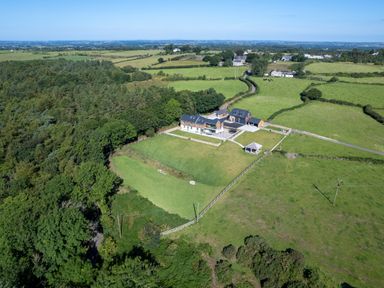Aerial view of a house with adjacent buildings and green fields near a forest at Rynys in Llanddeiniolen near Llanrug