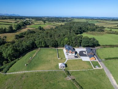 A property with a house, driveway, fenced lawn, and a gazebo surrounded by fields and trees at Rynys in Llanddeiniolen near Llanrug
