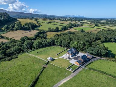 An aerial view of a house with surrounding green fields trees and a gazebo at Rynys in Llanddeiniolen near Llanrug